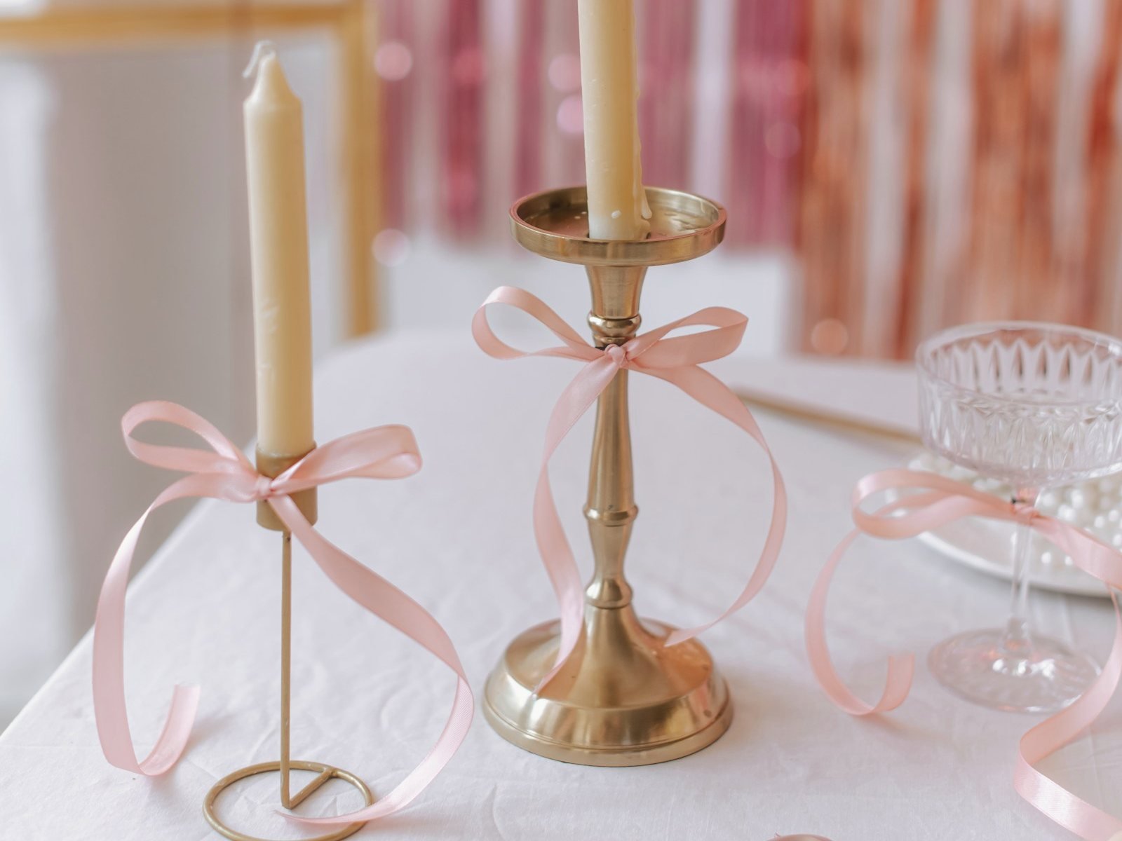 Bougeoirs dorés noués de rubans roses sur une nappe blanche